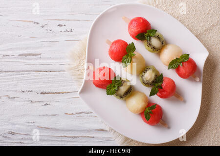 Brochettes de fruits avec des boules de pastèque, melon et kiwi sur une assiette. Vue supérieure horizontale Banque D'Images