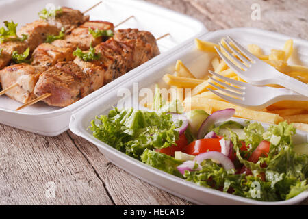 Fast food : Brochettes, frites et salade fraîche dans le bac sur la table horizontale. Banque D'Images