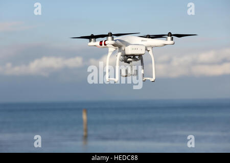 Drone télécommandé blanc Dji Phantom 3 équipé de caméra vidéo haute résolution planant dans l'air avec la terre et ciel bleu Banque D'Images