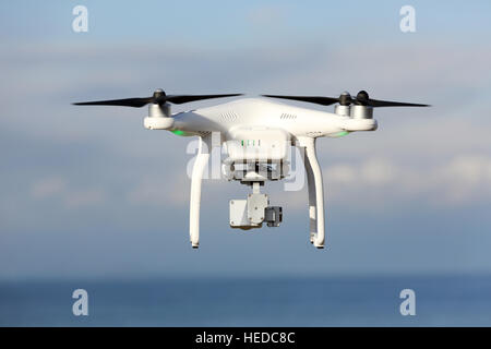 Drone télécommandé blanc Dji Phantom 3 équipé de caméra vidéo haute résolution planant dans l'air avec la terre et ciel bleu Banque D'Images