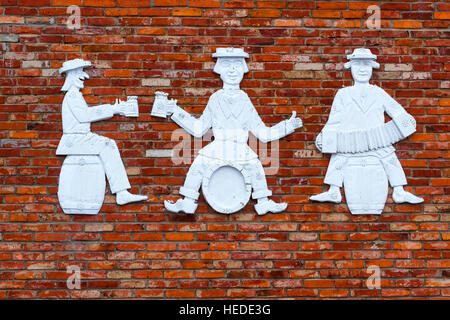 Figures de pierre de trois hommes sur mur de brique. Les gens d'humour sont assis sur des barils, boire de la bière et à l'harmonica. Countrysi provincial lituanien Banque D'Images