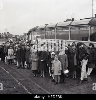 Historique des années 60, l'image montre un grand groupe de parents et leurs enfants en attente à l'extérieur de leur entraîneur sur le point d'entreprendre un travail ou d'entreprise. Banque D'Images