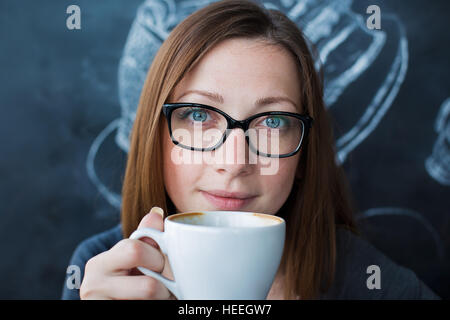 Girl holding a cup of coffee and looking at camera Banque D'Images