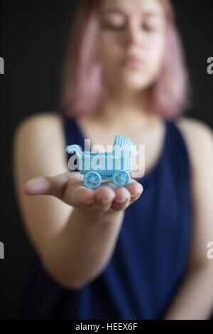 Une teen girl holding a baby carriage miniature dans la paume de sa main. Banque D'Images