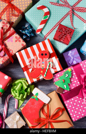 Tourné à angle élevé de certains biscuits de Noël et un tas de cadeaux enveloppés de papiers de nice et attachées avec des rubans de couleurs différentes sur un sol en bois rustique sur Banque D'Images