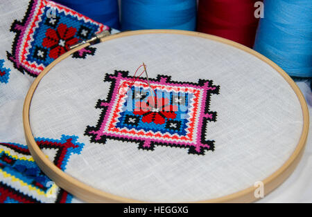 Folk traditionnel brodé motif géométrique, une croix sur un tissu blanc, à proximité d'un certain nombre de thread de couleur Banque D'Images