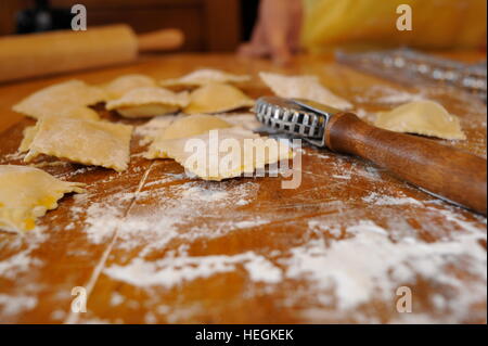 Raviolis maison faire des pâtes avec un cutter dans une cuisine, sur plancher couvert planche à découper en bois avec rouleau à pâtisserie en arrière-plan. Banque D'Images