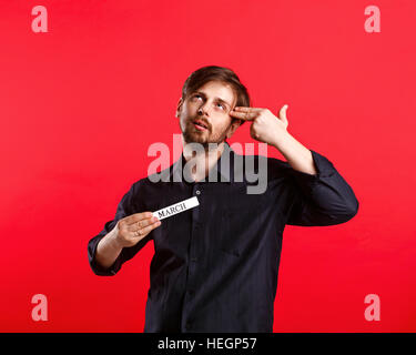 Man holding blank avec nom du mois de mars. L'homme abattu attrayant pour l'année civile. Il posa deux doigts sur sa tête comme si c'était une arme à feu. Banque D'Images