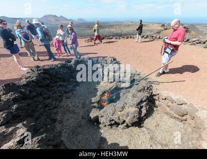 Les touristes regarder broussailles brûler dans un évent volcanique dans le Parc National de Timanfaya, Montañas del Fuego (Montagnes de Feu) dans Lazarote, Canaries, Espagne Banque D'Images