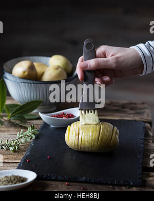 Hasselback potatoes : woman's hand le brossage une pomme de terre avec du beurre Banque D'Images