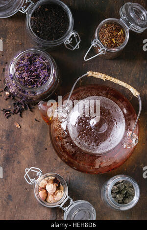 Variété de noir, vert et les feuilles de thé sèches dans des bocaux en verre avec crépine et vintage théière de thé chaud plus ancien en bois sombre arrière-plan. Vue d'en haut Banque D'Images