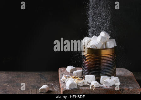 Tas de guimauve à la vanille fraîche et frit avec du sucre en poudre d'arrosage old tin can sur conseil en terre cuite sur fond de bois sombre. Copie Banque D'Images