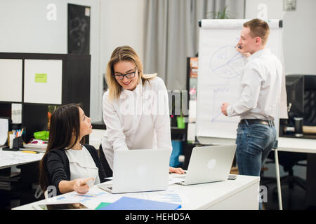Deux belles des employés de bureau ayant conversation tandis que l'homme collègue dimensions stratégie d'entreprise sur un tableau. Banque D'Images