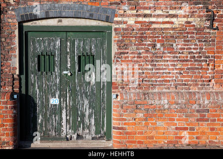 Vieux dock verrouillé les portes latérales assis dans un mur mal réparé. double porte avec fenêtre bars pour la sécurité et à l'écaillement de la peinture verte. Banque D'Images