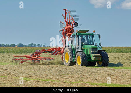 Un tracteur John Deere 6610 avec un râteau Kuhn à l'aide d'un rotor pour faire les petits andains pour accélérer le séchage du foin. Banque D'Images