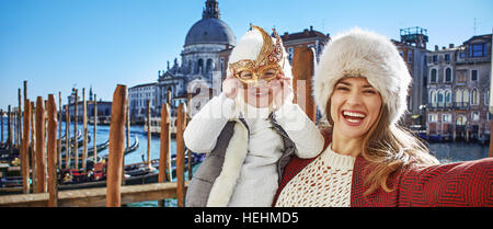 Un autre monde vacances. smiling trendy la mère et l'enfant du voyage à Venise, Italie prenant en selfies masque de Venise Banque D'Images