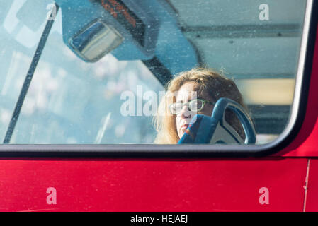 Une femme assise seule à l'avant de la partie supérieure d'un bus à impériale rouge, regarder par la fenêtre, alors qu'elle voyage à travers Londres. Banque D'Images