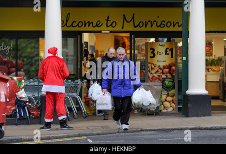 Brighton UK 23 décembre 2016 - Shoppers laden avec les sacs passent par une grande question vendeur habillé en père Noël lorsqu'ils quittent un supermarché Morrisons à Brighton avec aujourd'hui devrait être le jour de shopping de Noël le plus achalandé de la période des fêtes en Grande-Bretagne Crédit : Simon Dack/Alamy Live News Banque D'Images