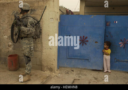 Un soldat de l'armée américaine de la compagnie B, 1er bataillon, 23e régiment d'infanterie, 3e Stryker Brigade combat Team, 2e division d'infanterie a assuré la sécurité lors d'une opération de cordon et de recherche devant une maison à Rashid, en Irak, le 3 mai 2007, observé par un garçon local. Banque D'Images