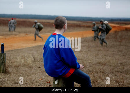 Un enfant regarde comme parachutistes américains de revenus après avoir rempli leur saut dans la participation à la 17e édition de Randy Oler Opération Memorial Toy Drop, organisé par l'armée américaine et des affaires civiles de la commande d'opérations psychologiques (Airborne), le 6 décembre 2014 sur la zone de la Sicile à Fort Bragg, Caroline du Nord. Jouet opération Drop est la plus grande opération aéroportée combiné avec six pays partenaire alliées participant parachutistes et permet aux soldats la possibilité d'aider les enfants dans le besoin tout au long de la communauté locale de recevoir des jouets pour les fêtes. (U.S. Photo de l'armée par la CPS Ashley Keasler ) opération Toy Banque D'Images