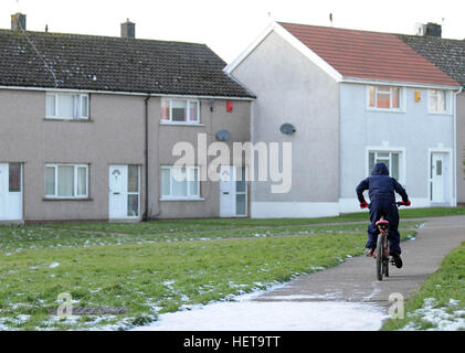 Un garçon cycles sur un chemin couvert de neige sur le Gurnos logement Conseil estate dans Merthyr Tydfil, South Wales, UK. Banque D'Images