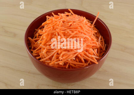 Carottes râpées dans red bowl on wooden table Banque D'Images