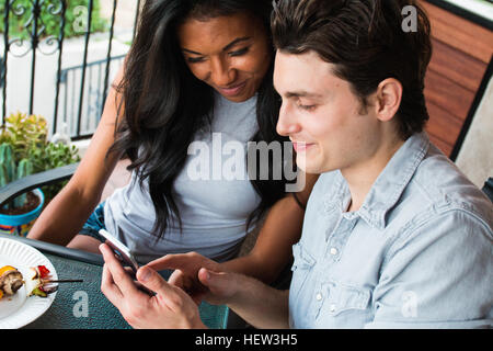 Jeune couple assis sur la véranda, looking at smartphone Banque D'Images