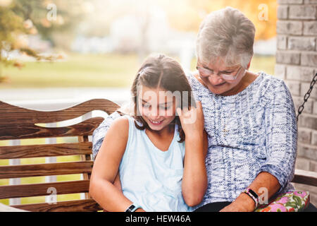 Grand-mère et petite-fille assise sur porche swing, rire Banque D'Images