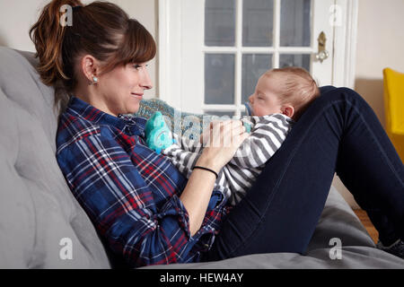 Mother sitting on sofa looking à sleeping baby boy, smiling Banque D'Images