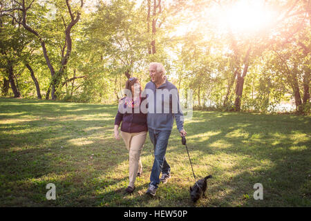 Romantic senior couple walking the dog in sunlit park Banque D'Images