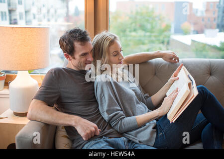 Couple reclining on sofa reading a book Banque D'Images