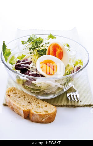 Salade composée d'œufs, de chou blanc, la laitue, la chicorée et le cresson dans un bol en verre sur un set de table à côté d'une fourchette et tranche de Banque D'Images