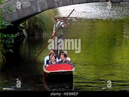 Un parieur à Christchurch accueille les passagers à bord d'un bateau à fond plat pour une expérience de punting traditionnelle sur la rivière Avon. Le punting, une activité touristique populaire, consiste à utiliser un bâton pour pousser le bateau le long de la rivière, offrant une vue panoramique sur les rues et l'architecture de la ville. Banque D'Images