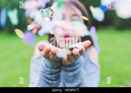 Close up of young woman in park soufflant poignée de confettis Banque D'Images