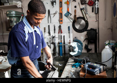 Jeune homme à l'aide d'une pince en atelier de réparation Banque D'Images
