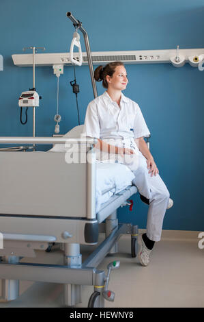 Nurse sitting on hospital bed looking away Banque D'Images