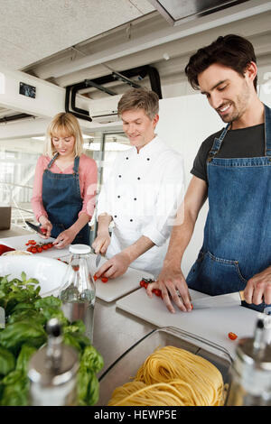 Chef et couple in kitchen slicing tomatoes Banque D'Images