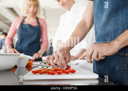 Chef et couple in kitchen slicing tomatoes Banque D'Images