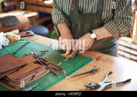 Travailleur homme cuir en atelier, contrôle de la netteté du couteau sur le cuir, mid section Banque D'Images