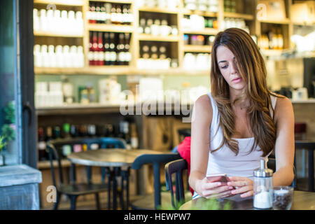 Young woman sitting in cafe lecture textes smartphone Banque D'Images