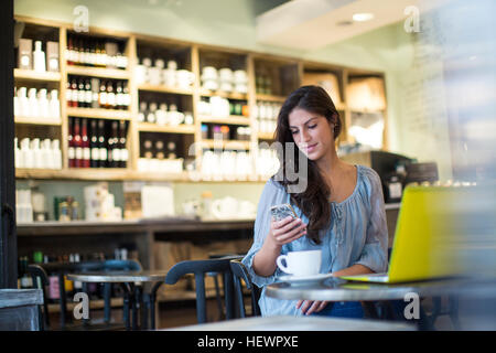 Jeune femme lisant des textes dans smartphone cafe Banque D'Images