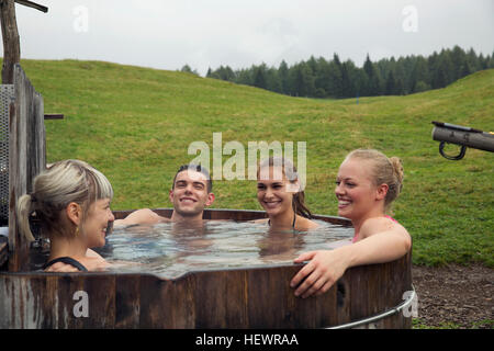 Quatre amis adultes rire tout en vous relaxant dans le bain à remous, Sattelbergalm rural, Tyrol, Autriche Banque D'Images