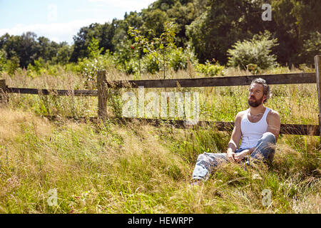 Mid adult man sitting contre regardant Clôture rurale Banque D'Images