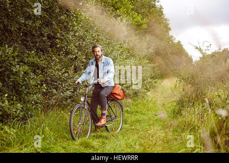 Portrait of mid adult man on bicycle sur chemin rural Banque D'Images