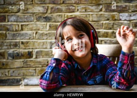 Happy boy sitting at table listening to headphones Banque D'Images