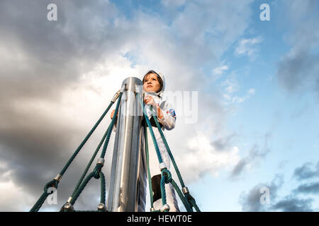 Garçon en costume d'astronaute regardant haut de escalade contre ciel dramatique Banque D'Images