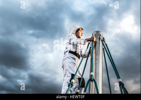 Garçon en costume d'astronaute contemplant du haut du mur d'escalade contre ciel dramatique Banque D'Images