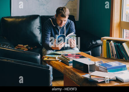 Mid adult man sitting in chair, à l'entremise des livres Banque D'Images