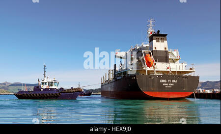 Le remorqueur Blackadder assiste le cargo XING Yi HAI dans le port de Lyttleton, en Nouvelle-Zélande. Le XING Yi HAI, d'une jauge brute de 24 991 et immatriculé à Hong Kong, transporte activement des marchandises. Cette image illustre l'assistance et l'activité maritime du navire. Banque D'Images