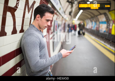 Vue de côté de l'homme sur un quai de gare looking at smartphone Banque D'Images